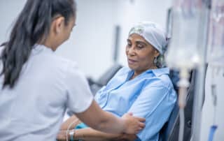 A woman wearing a head scarf recovers from chemo treatment in the hospital. A doctor speaks with her and offers her support.